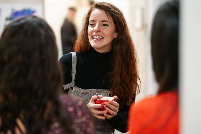 Woman holding red coffee cup chatting with friends