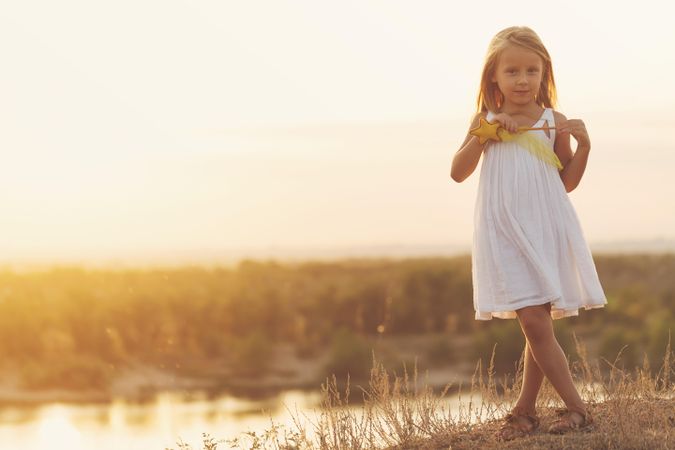 Blonde female child in summer dress standing in front of lake