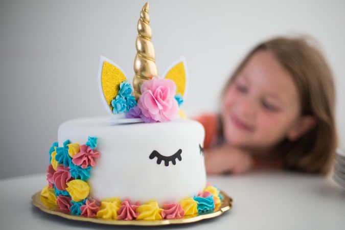 Bright unicorn cake for pleased girl at table
