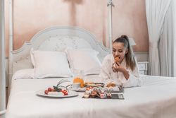 Woman in bathrobe laying forward and having a breakfast on bed