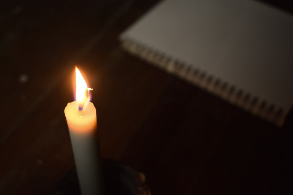 Top view of candle lit in the dark next to notebook