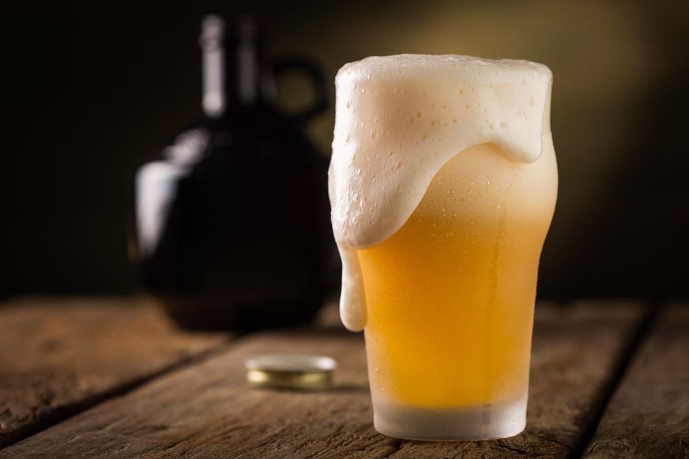 Side view of freshly poured pint of beer overflowing with foam