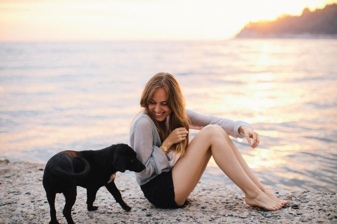 Woman sitting beside puppy on beach during sunset