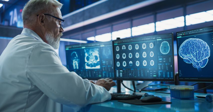 Male Neuroscientist Using Desktop Computer To Analyze MRI Scans Of Brain In Medical Research Center Laboratory.