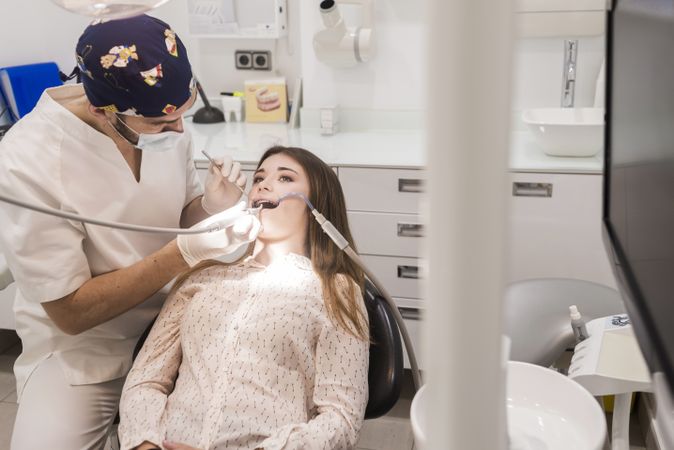 Masked male dentist working on mouth of female teenage patient