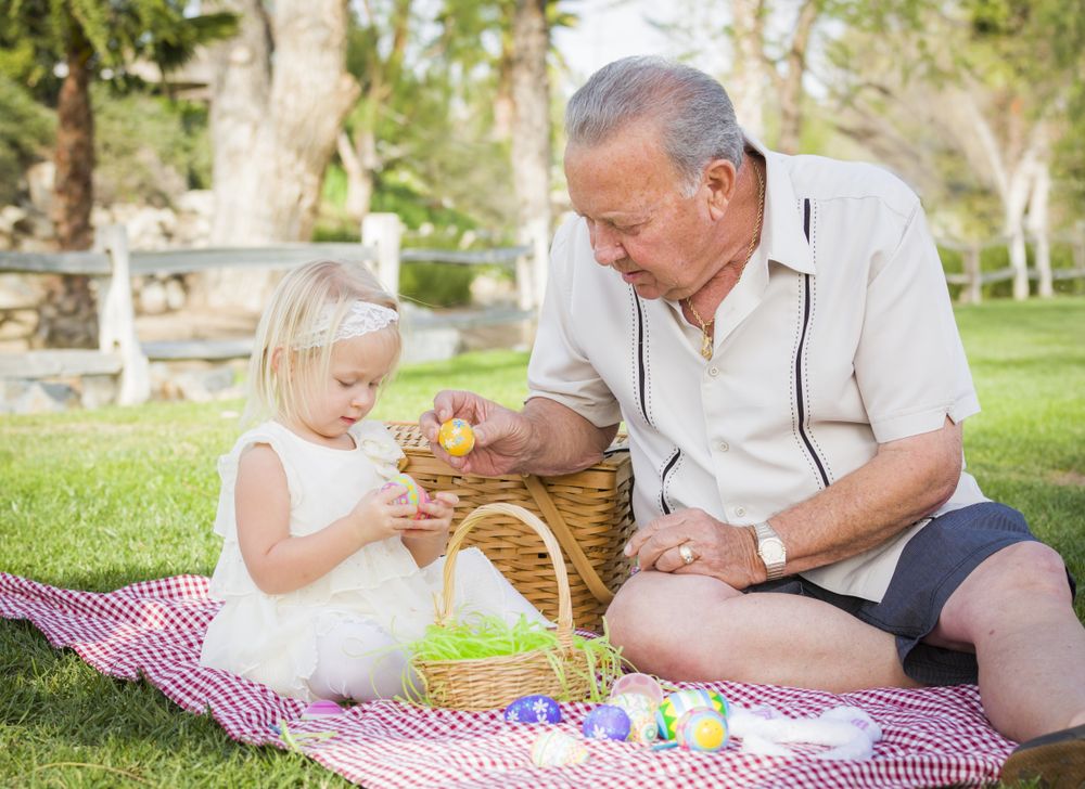 Grandfather and Granddaughter Enjoying Easter Eggs on Blanket At Park