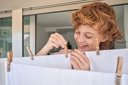 Adorable smiling curly haired boy using clothespins for hanging