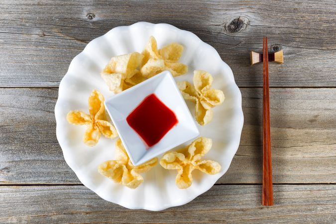 Fried wanton shells and sweet dipping sauce in bowl on rustic wood