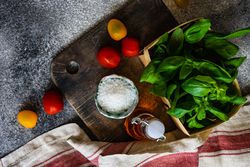 Top view of fresh basil, cherry tomatoes, salt and oil on bread board