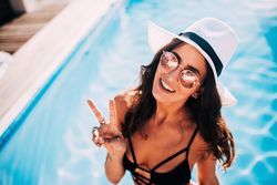 Young woman making peace sign on a sunny day by the pool