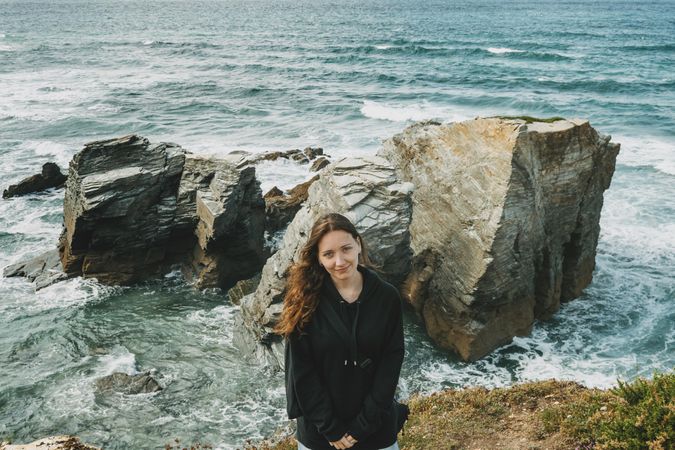 Smiling woman in dark jacket standing on the beach of Ribadeo, Lugo, Spain