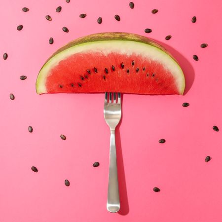 Composition with watermelon slice, fork and seeds on pink background
