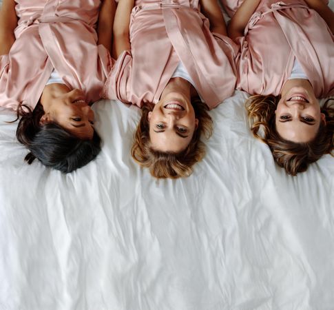 Top view of bride with female friends lying on bed and smiling