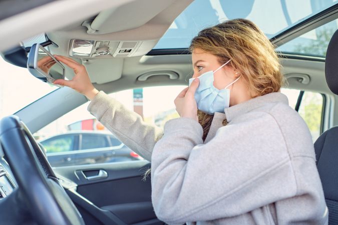 Woman putting on sterile mask against car mirror