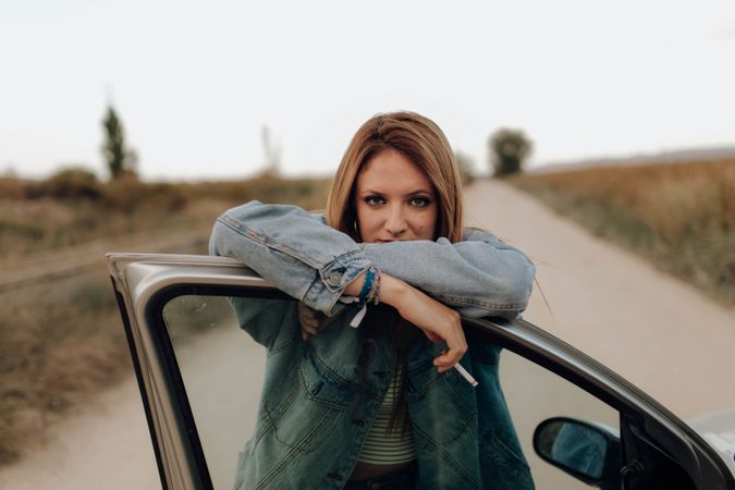 Modern woman with cigarette near car in nature