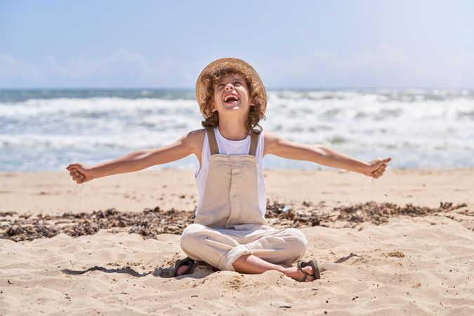 Cheerful boy sitting on sandy beach near ocean