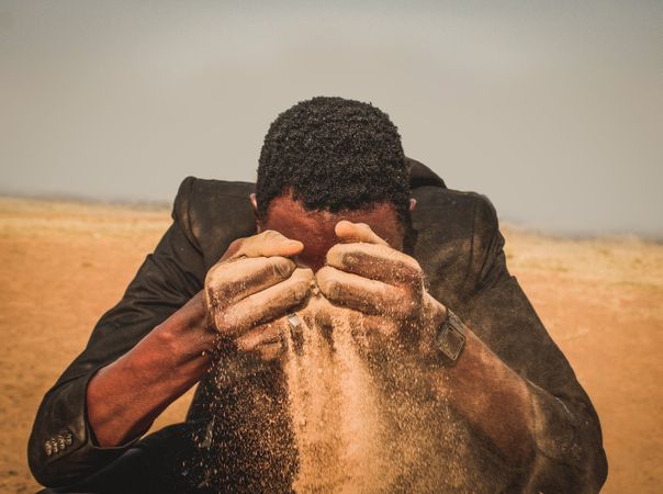 Man in dark suit unleashing sand from his hands