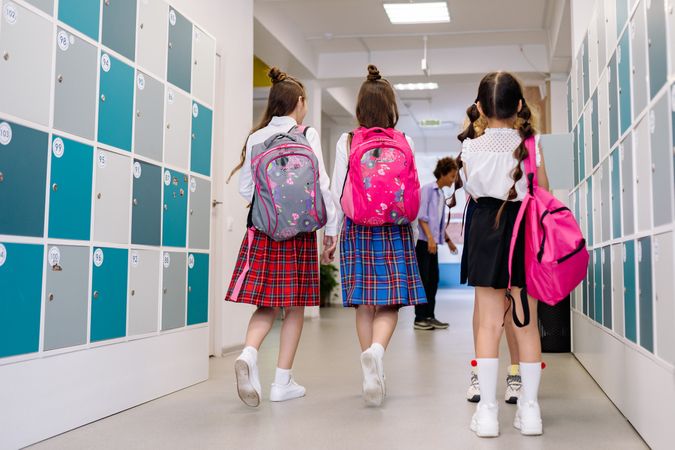 Back view of three girls in school uniform walking in hallway