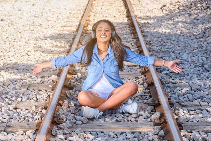 Smiling woman listening to music sitting on railroad