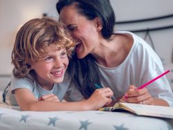 Cheerful boy and happy mother painting together lying on bed