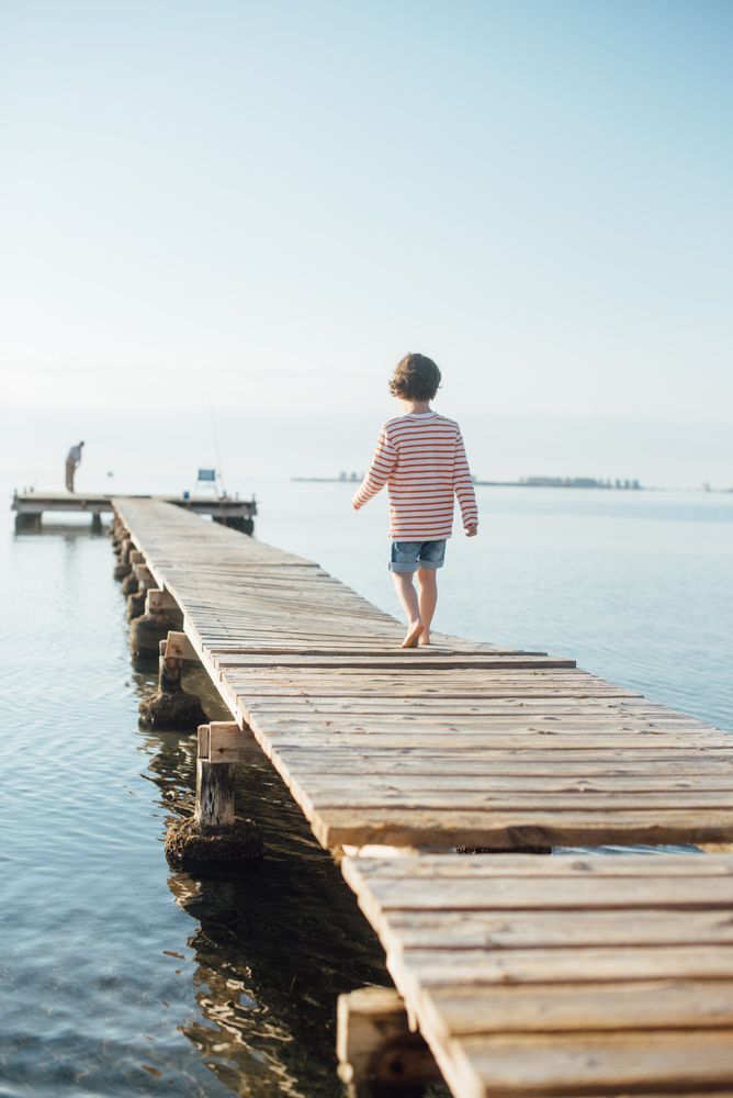 Lonely kid on pier in sunshine