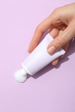 A jar of hand cream on a light, purple background.