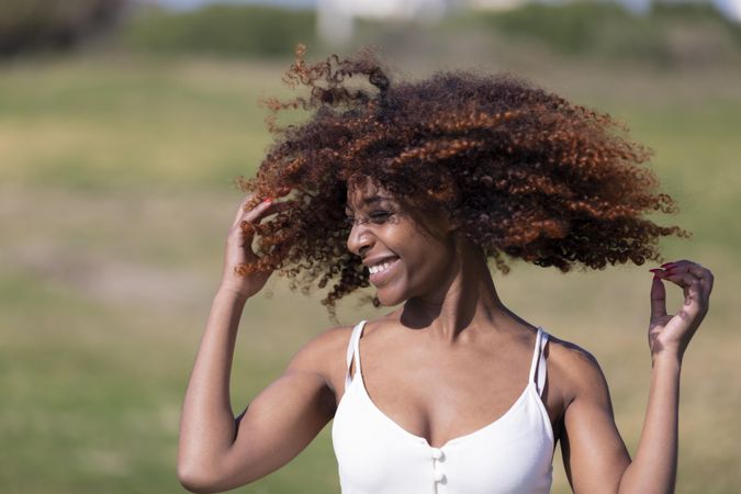 Female pictured outside in park playing with her curly hair