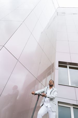 Black man in suit on electric scooter in business center
