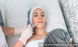 Aesthetician's hand's in latex gloves injecting botox into female's lips in a beauty salon 4d8ePl