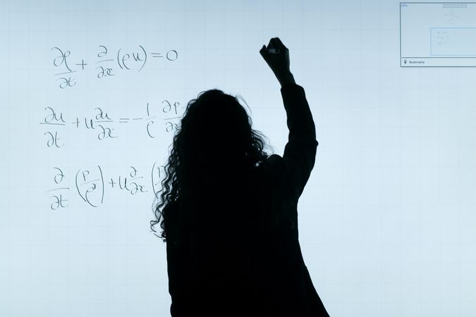 Back view silhouette of a math teacher writing on light board in classroom