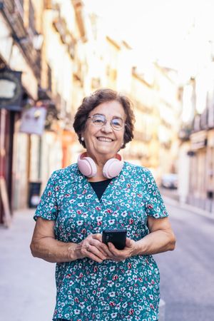 Older woman using smartphone and headphones walking down the street