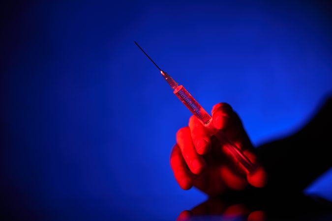 Crop person with syringe in neon lighting