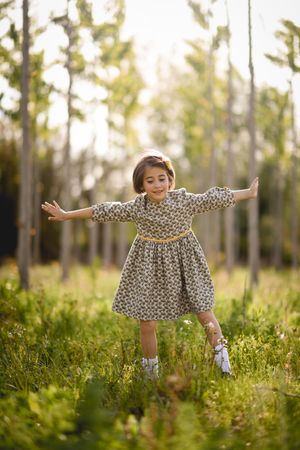 Happy child standing in dress in field surrounded by trees, vertical