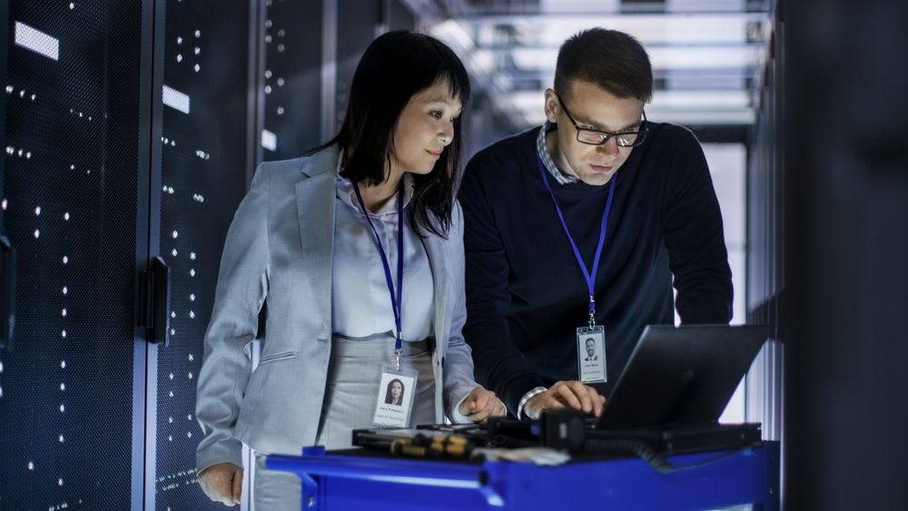 Male and Asian Female IT Technicians Working with Computer Crash Cart in Big Data Center full of Rack Servers.
