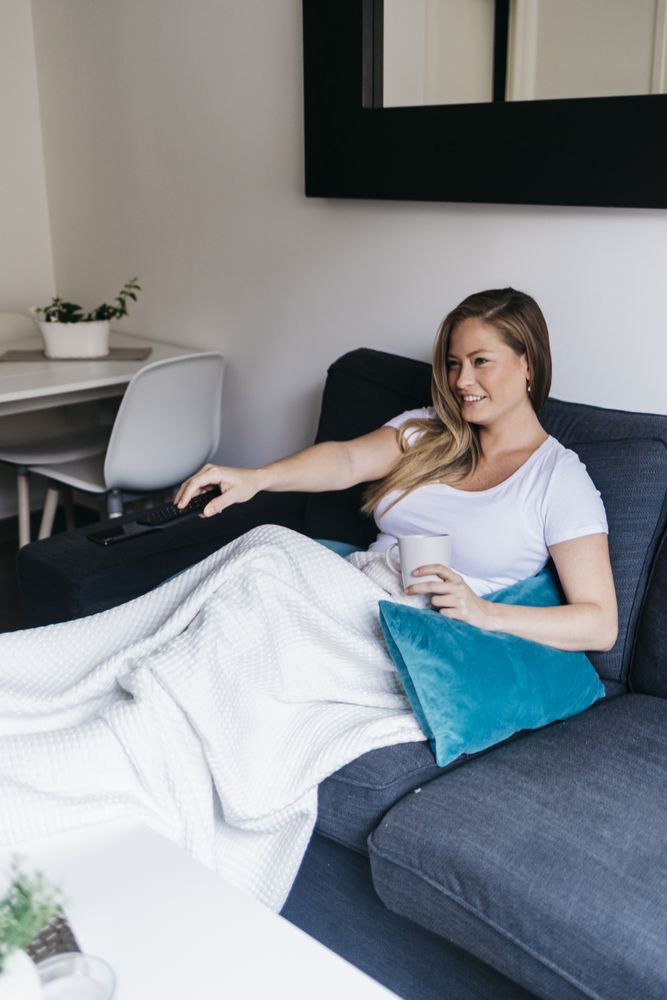 Cheerful young woman sitting on a couch at home watching tv