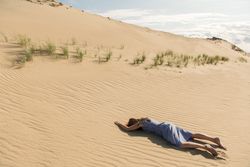 Young woman lying down on sand dune