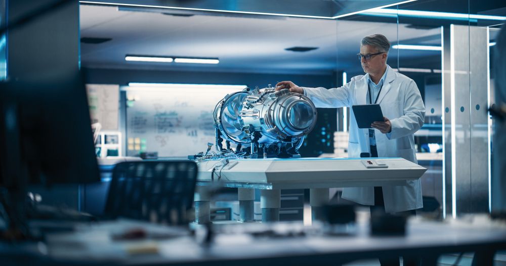 Jet Engine Specialist Working on a Project with Futuristic Turbine Motor, Standing with Tablet Computer in Scientific Technology Lab.