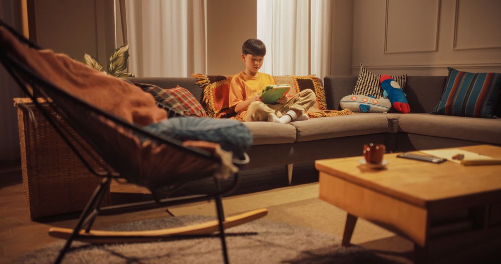 Portrait of a Focused Korean Male Kid Using Digital Tablet in the Living Room at Home.