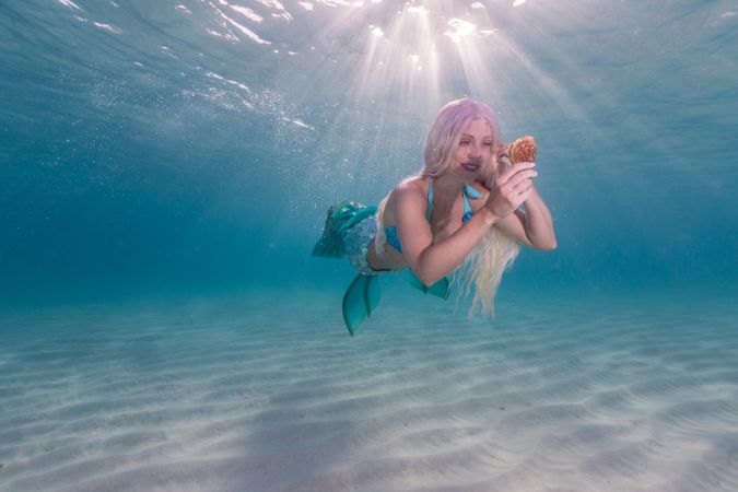 Blond fairytale female mermaid exploring underwater