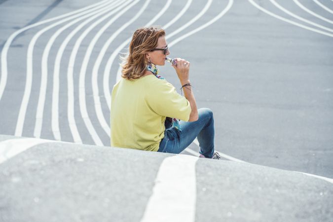Modern relaxed woman vaping while sitting on marked road