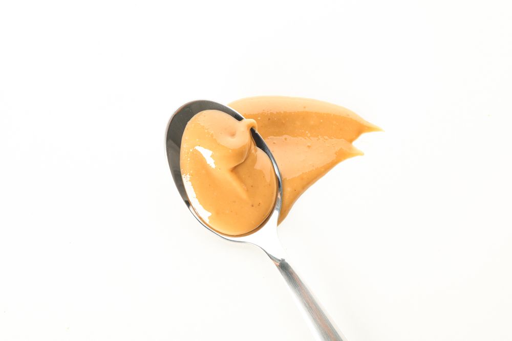 Spoon with creamy peanut butter isolated on light background, top view. A traditional product of American cuisine