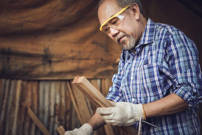 Mature male working in wood shop while wearing safety glasses