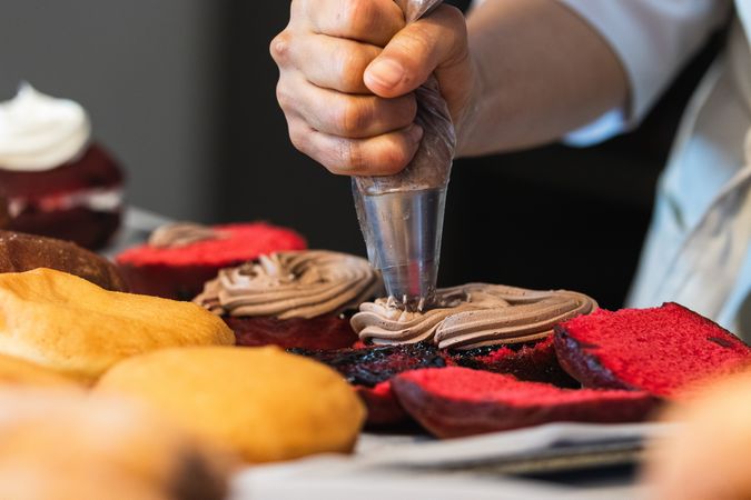 Unrecognizable baker adding cream on cakes in kitchen