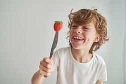 Cheerful boy looking at knife with strawberry on top
