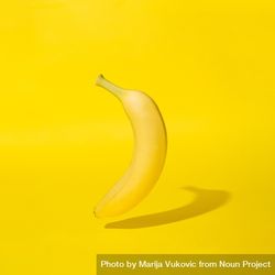 Single banana on yellow background with shadow 0VYDYb