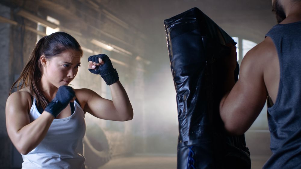 Athletic Woman Trains Her Punches on a Punching Bag that Her Partner  Trainer Holds.