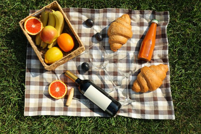 Composition with wine, croissants, fruits and towel on grass, top view