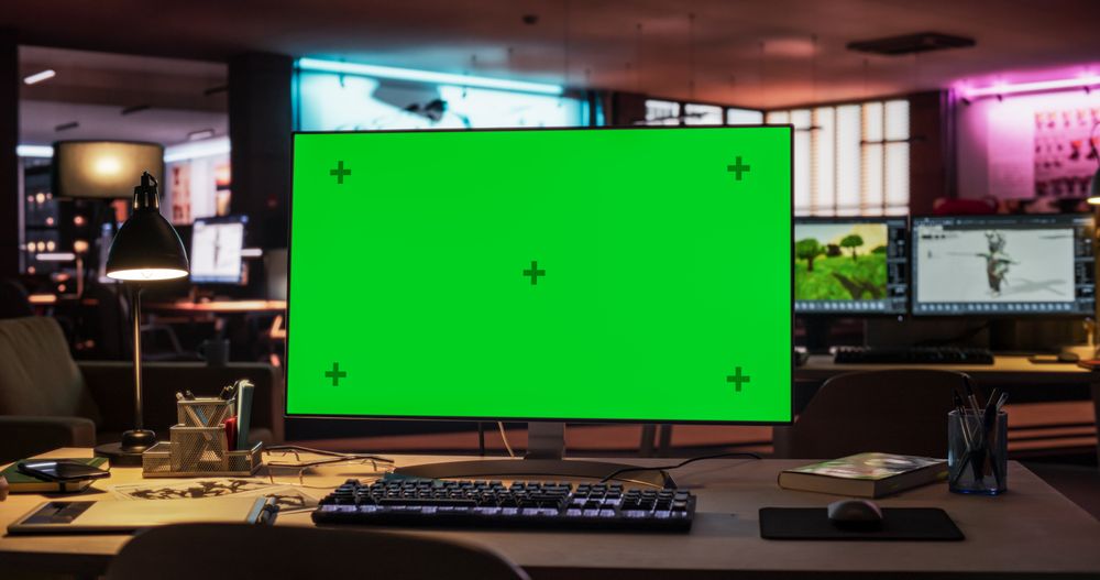 Desktop Computer Monitor Standing on a Wooden Desk with a Green Screen Chromakey Mock Up Display.