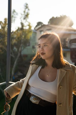 Fashionable young woman with straight brown hair and tan jacket on patio