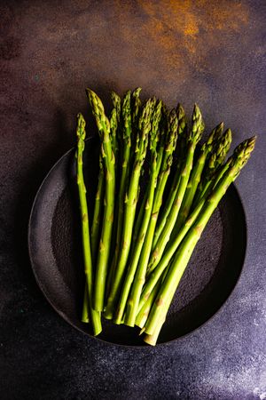 Raw asparagus on dark plate and dark counter